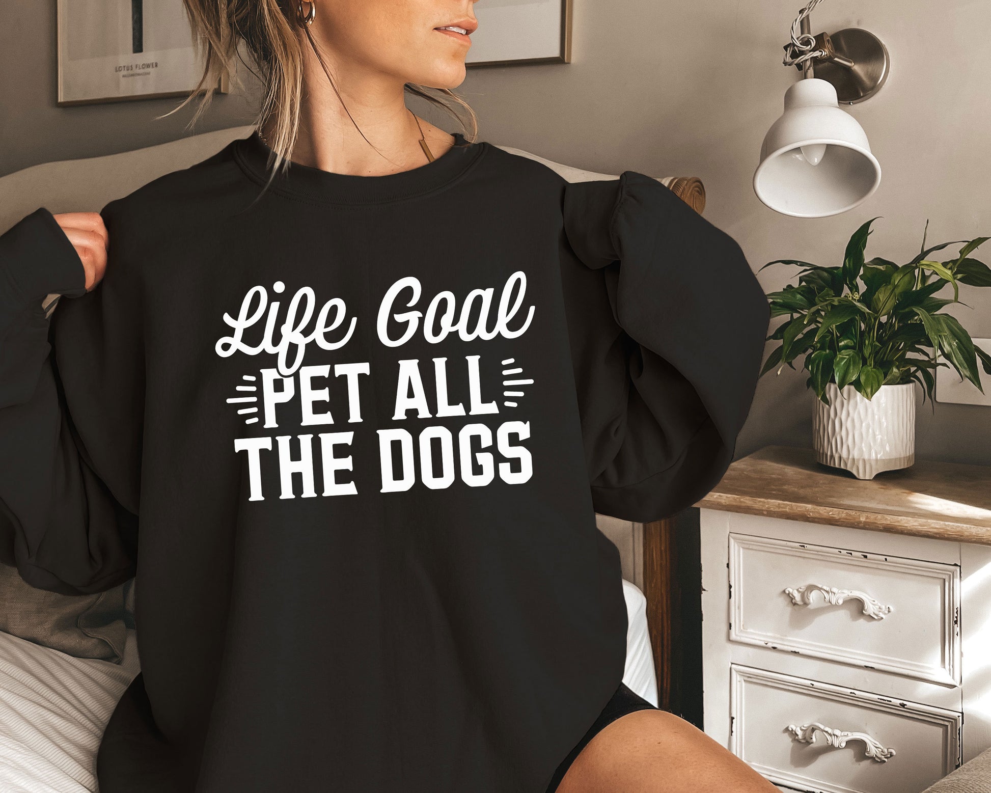 a woman sitting on a bed wearing a black shirt that says life goal pet all