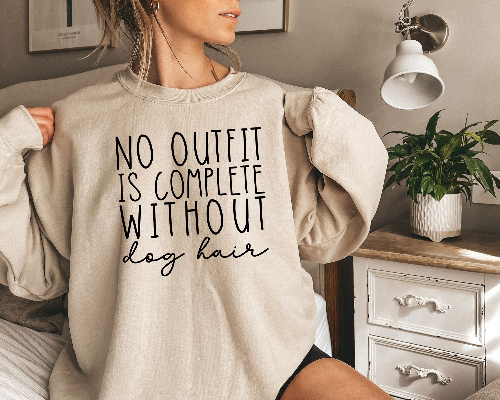 a woman sitting on a bed wearing a sweatshirt that says no outfit is complete without