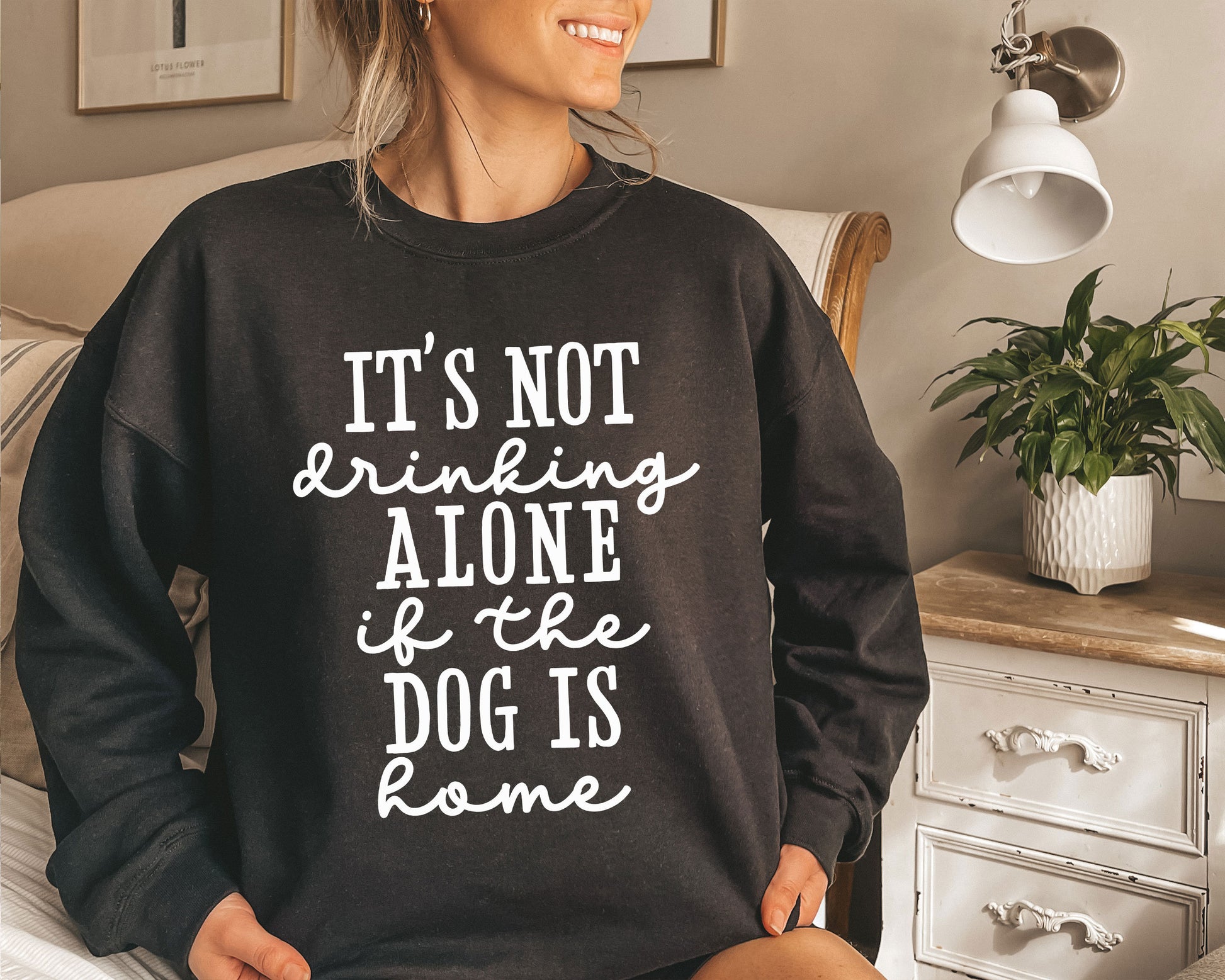 a woman sitting on a bed wearing a black sweatshirt that says it&#39;s not