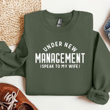 a green sweater that says under new management speak to my wife