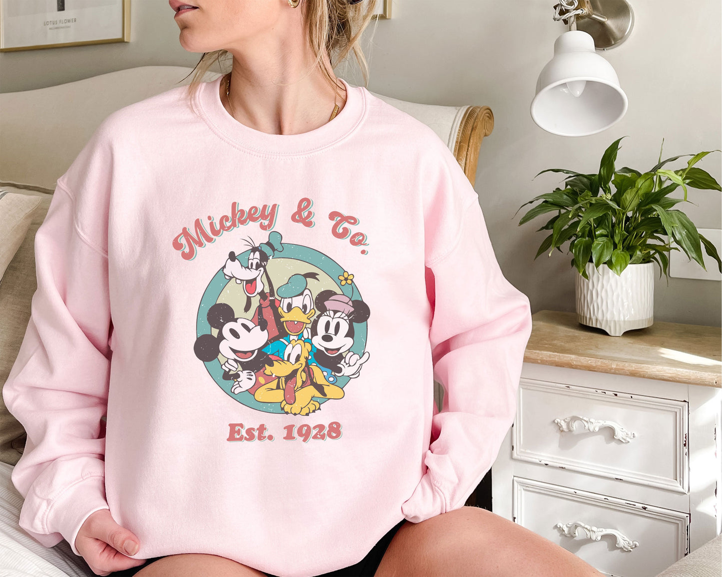 a woman sitting on a bed wearing a pink mickey mouse sweatshirt