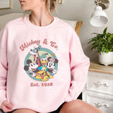 a woman sitting on a bed wearing a pink mickey mouse sweatshirt