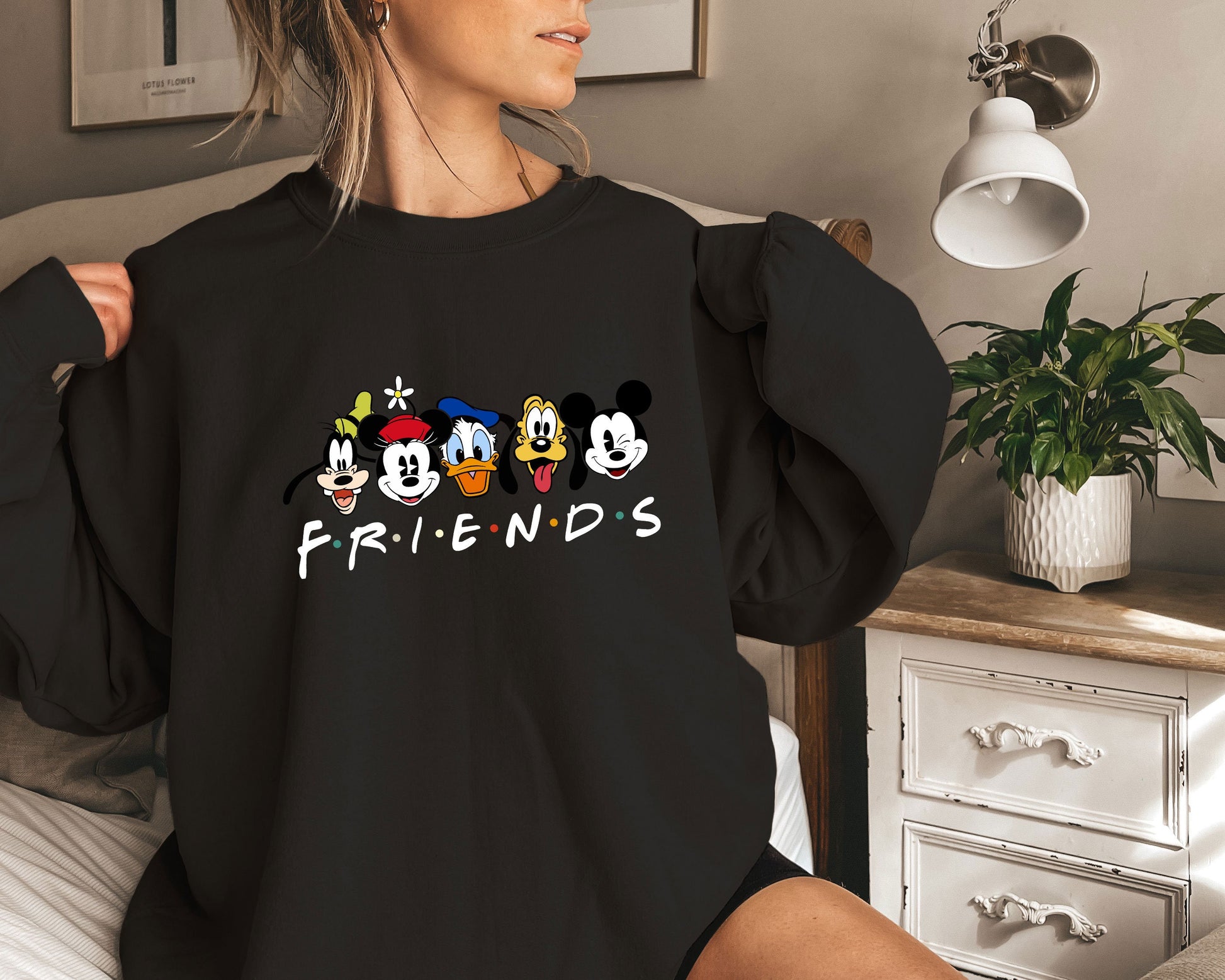 a woman sitting on a bed wearing a black shirt with mickey mouse friends on it