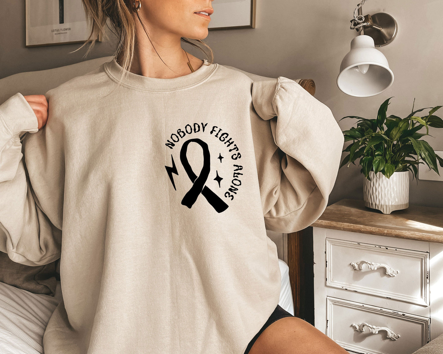 a woman sitting on a bed wearing a sweatshirt