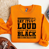 an orange sweatshirt that says say it's loud in black and a pair of