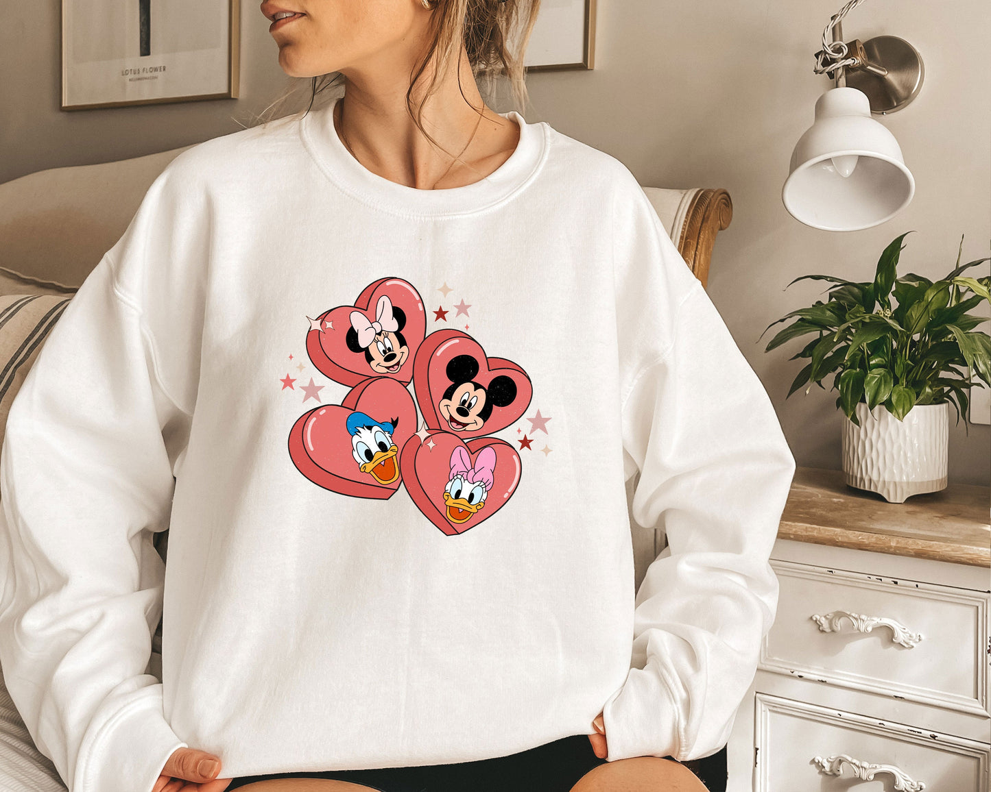 a woman sitting on a bed wearing a mickey mouse sweatshirt