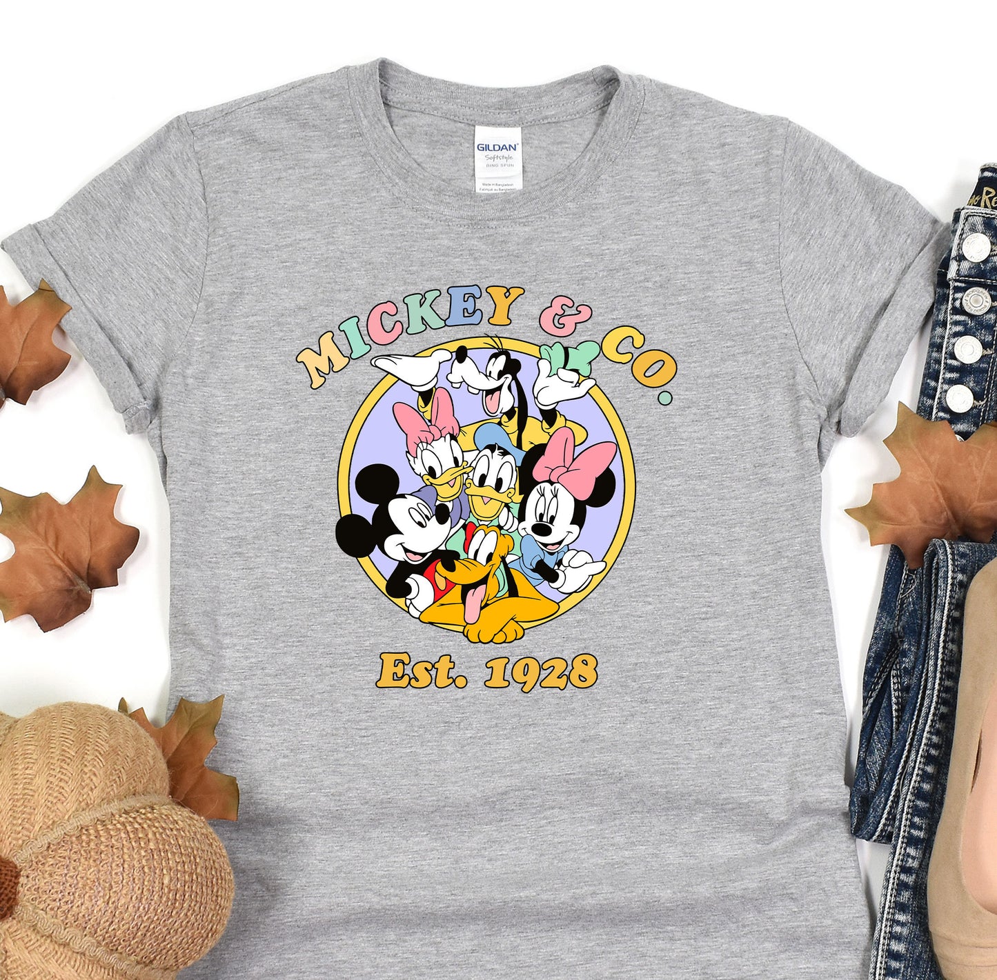 a mickey mouse t - shirt sitting on top of a pile of leaves