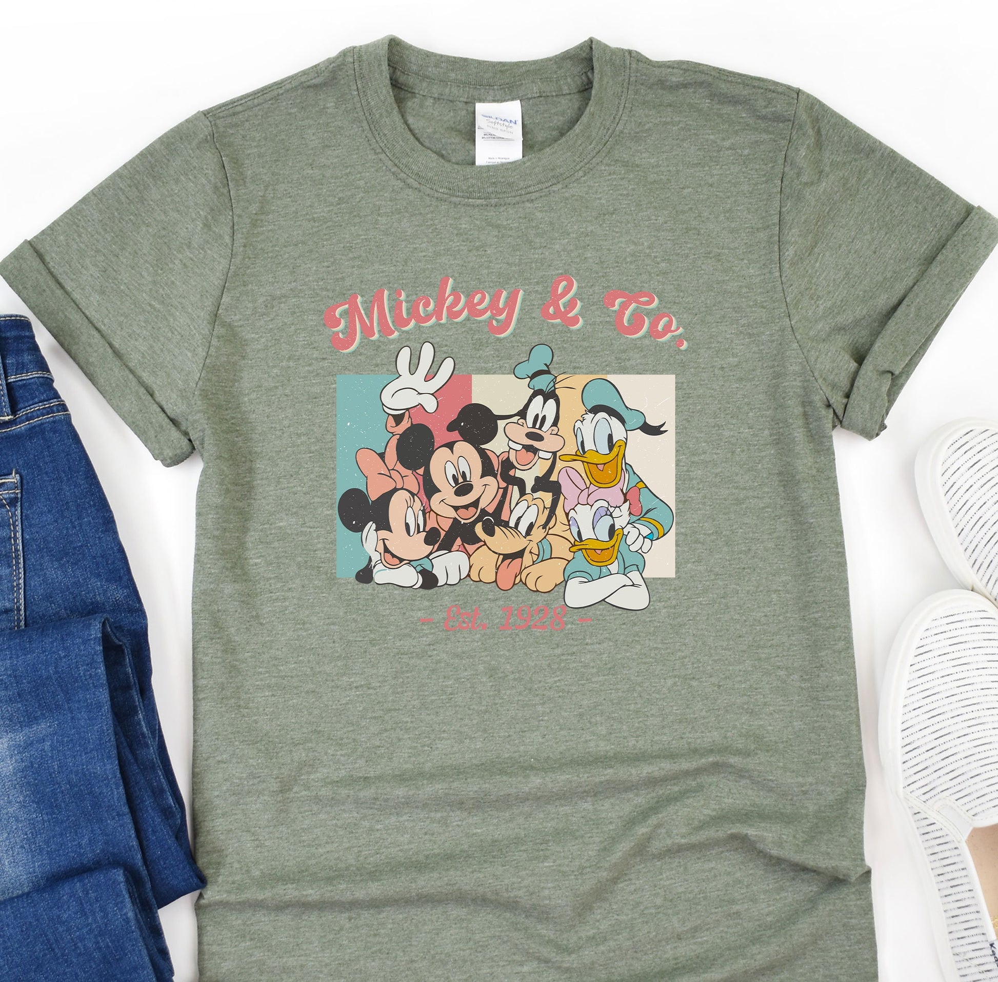 a mickey mouse and friends t - shirt sitting on top of a pair of jeans