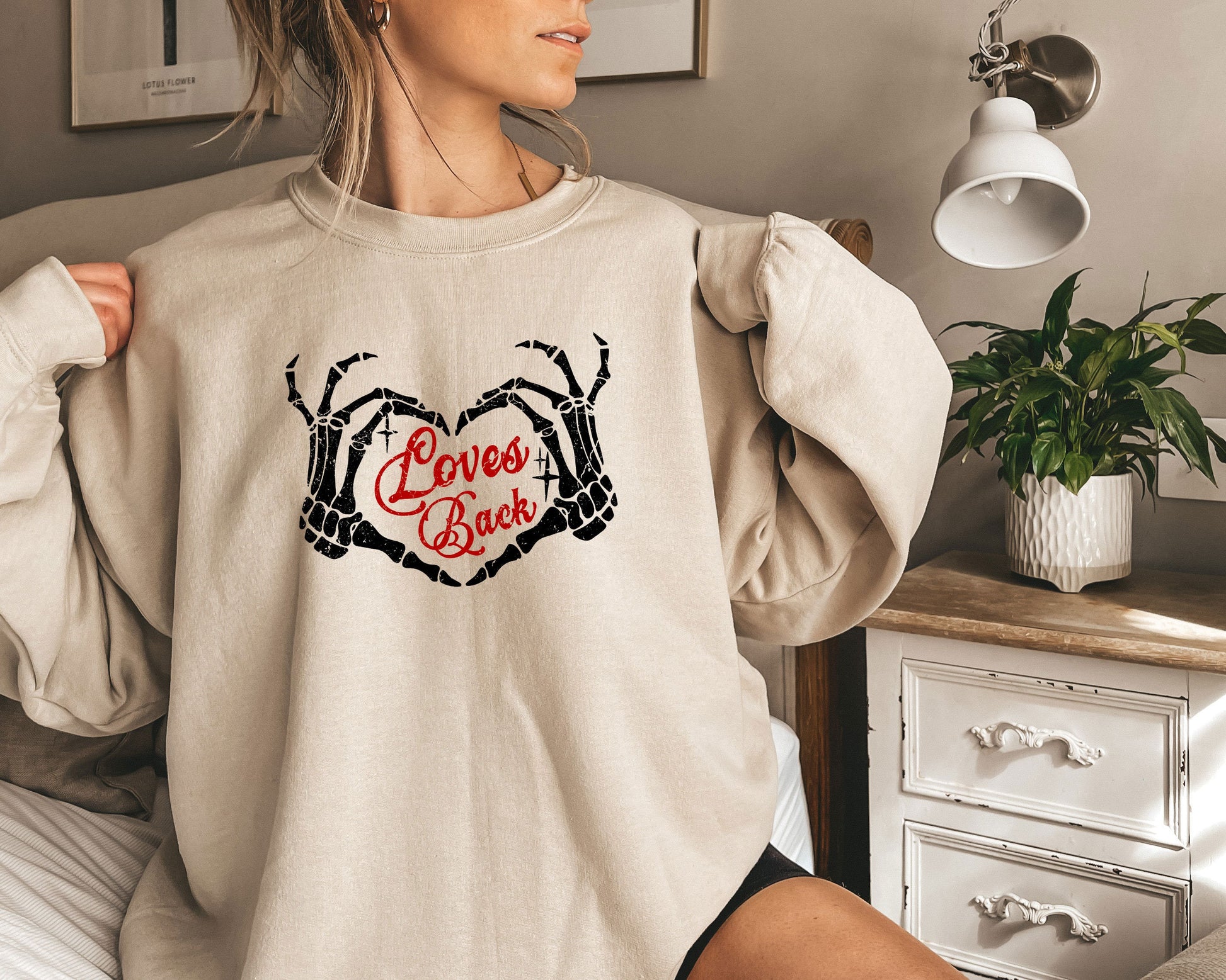 a woman is sitting on a bed wearing a sweatshirt