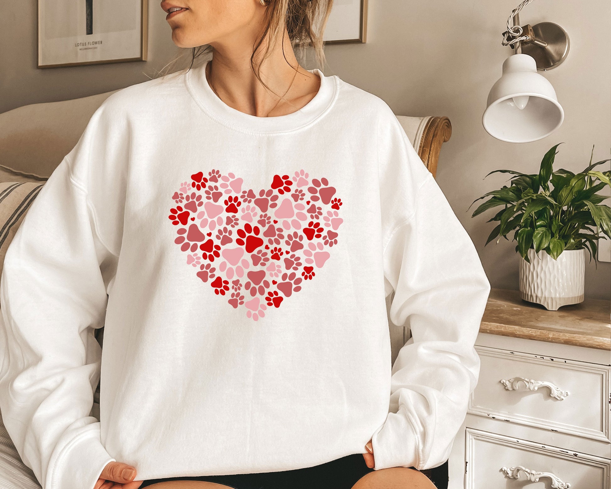 a woman sitting on a bed wearing a sweatshirt with a heart made of paw prints