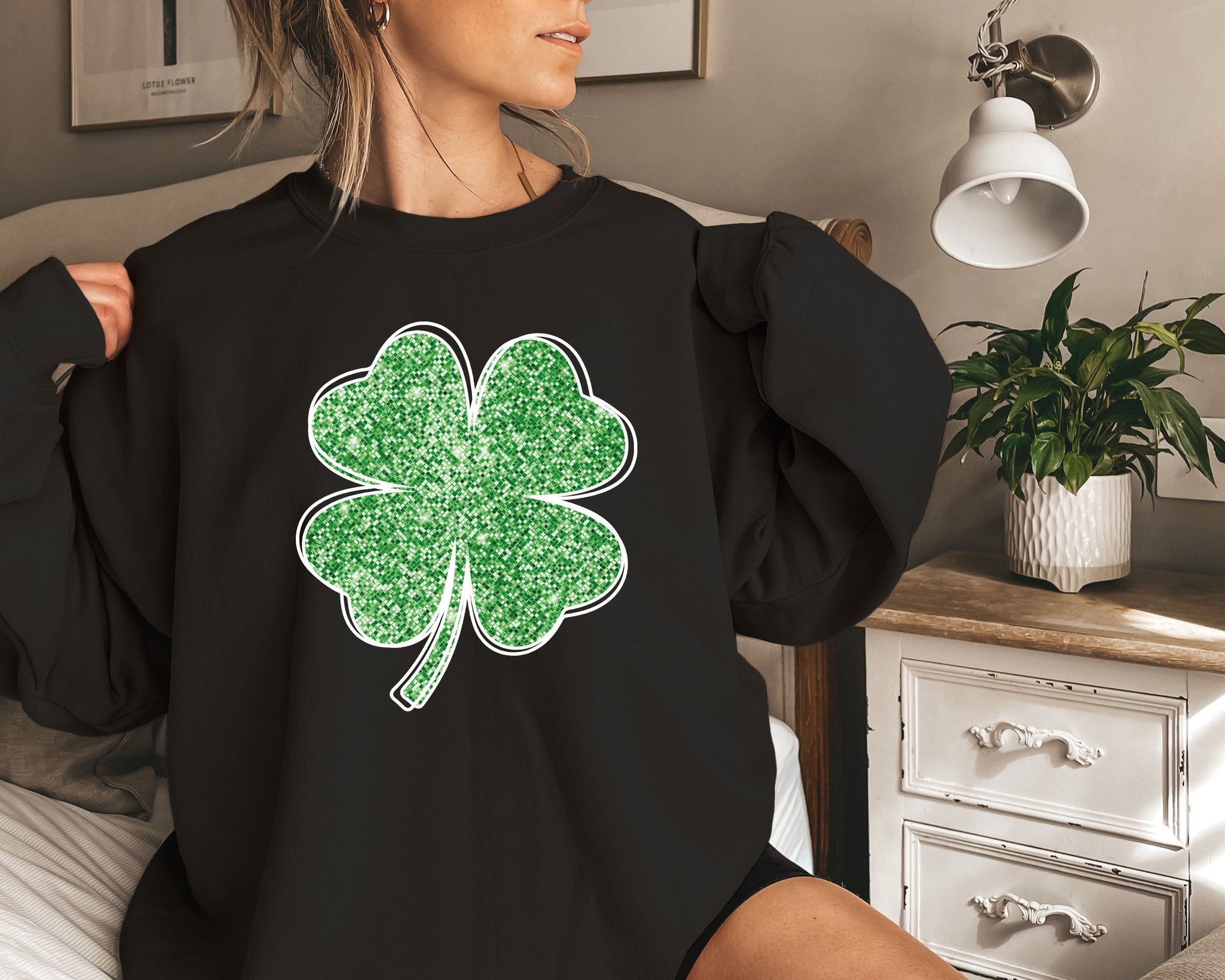 a woman sitting on a bed wearing a black shirt with a green clover on it