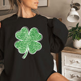 a woman sitting on a bed wearing a black shirt with a green clover on it