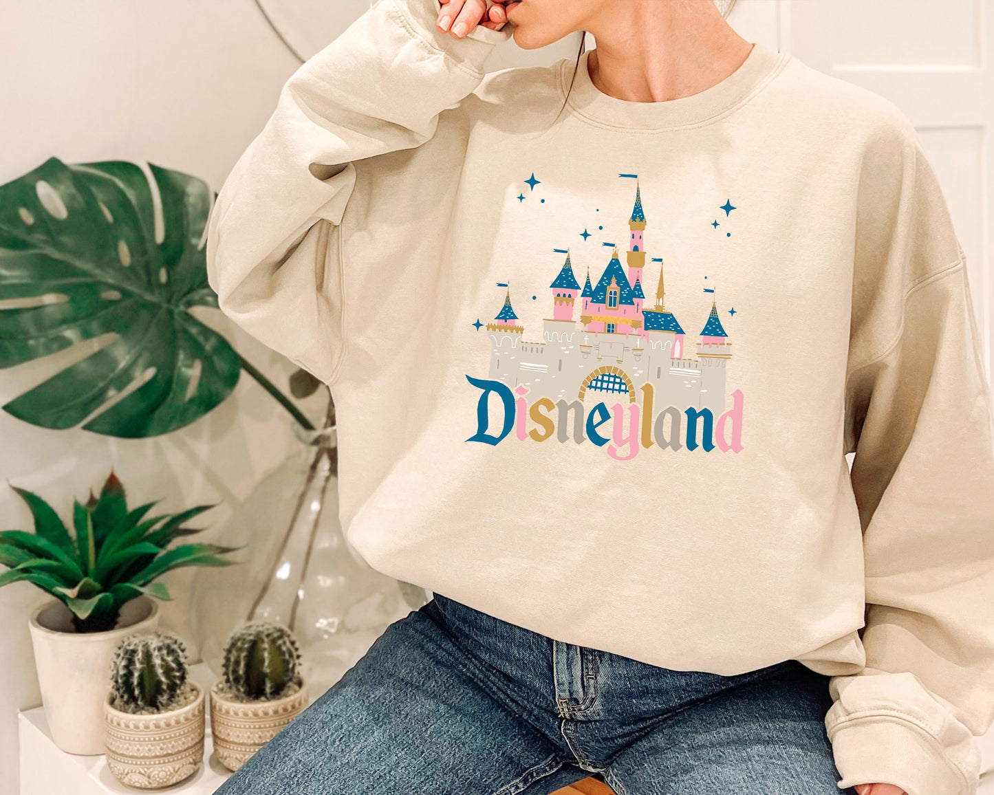 a woman sitting on a stool wearing a disneyland sweatshirt