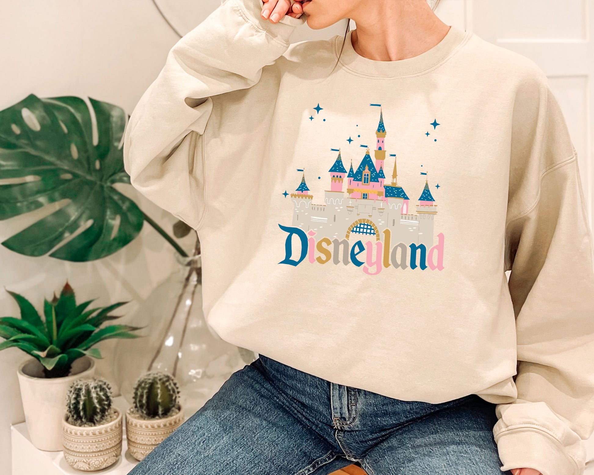 a woman sitting on a stool wearing a disneyland sweatshirt