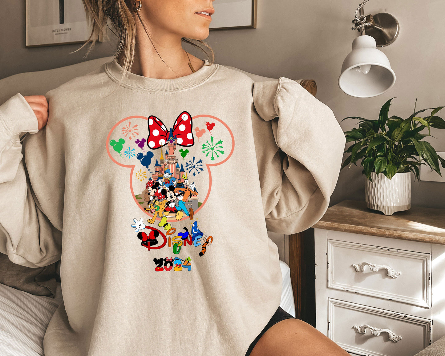 a woman wearing a mickey mouse sweatshirt standing on a bed