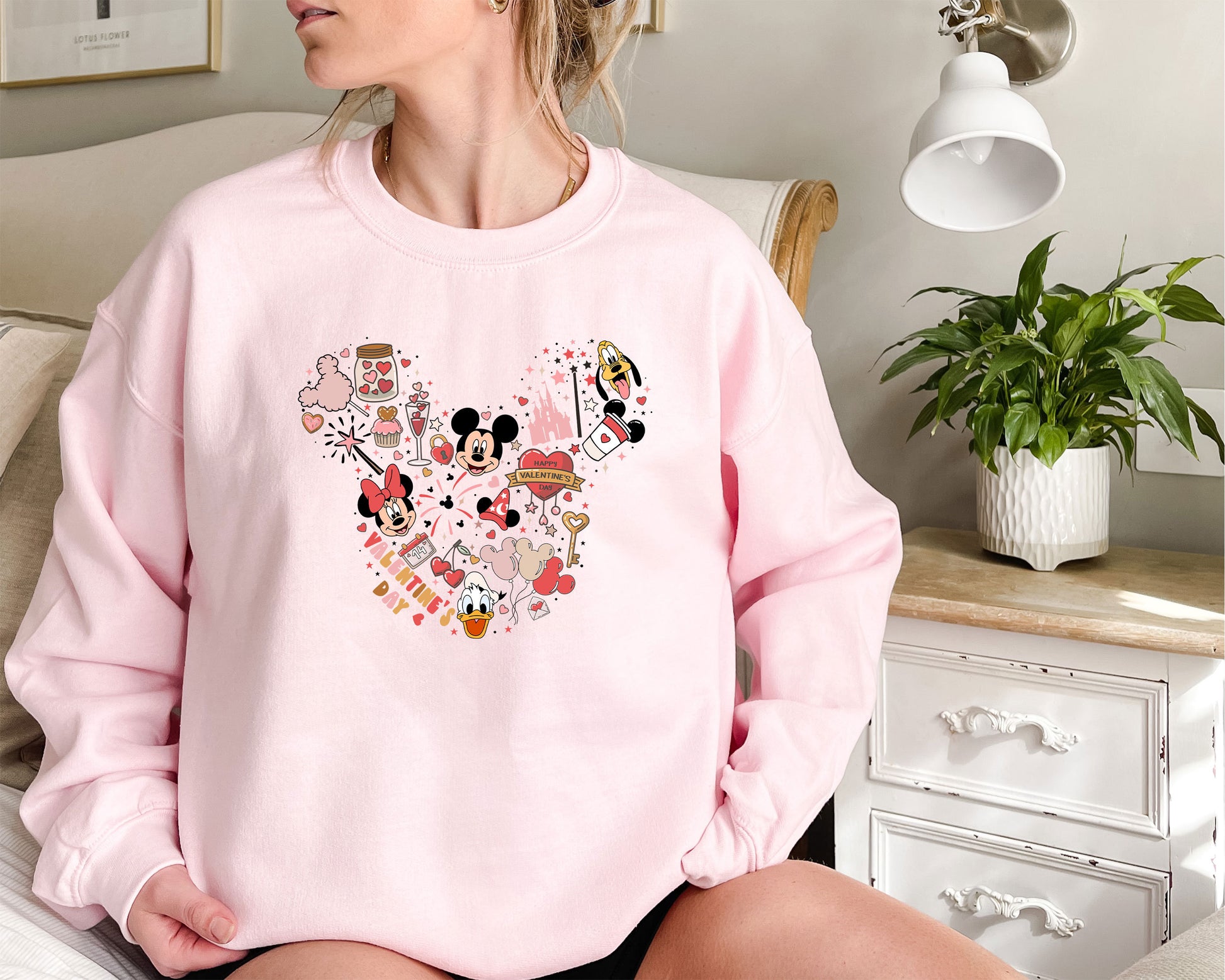 a woman sitting on a bed wearing a pink mickey mouse sweatshirt