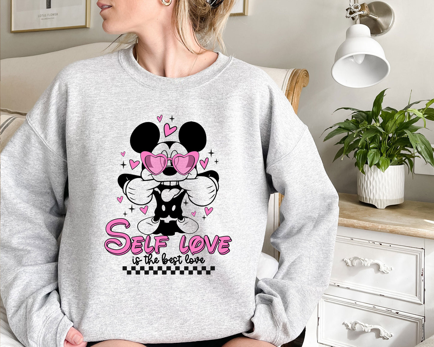 a woman sitting on a bed wearing a mickey mouse sweatshirt