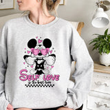 a woman sitting on a bed wearing a mickey mouse sweatshirt