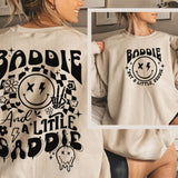 a woman wearing a sweatshirt that says baddie and a little saddie